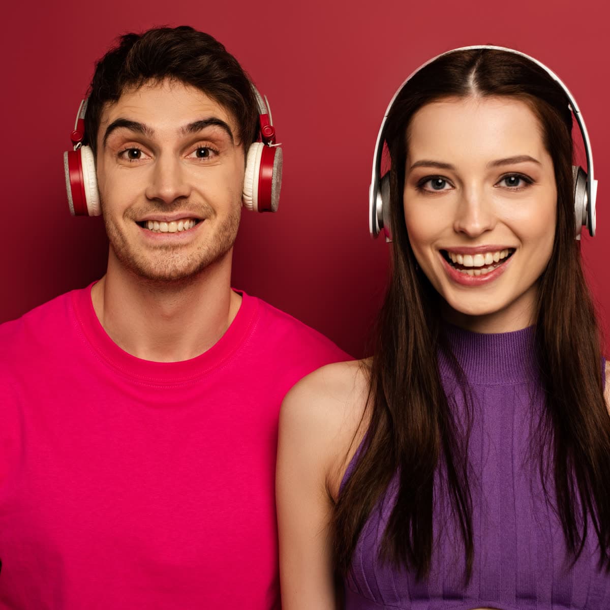 Smiling pair wearing headphones on a red studio background
