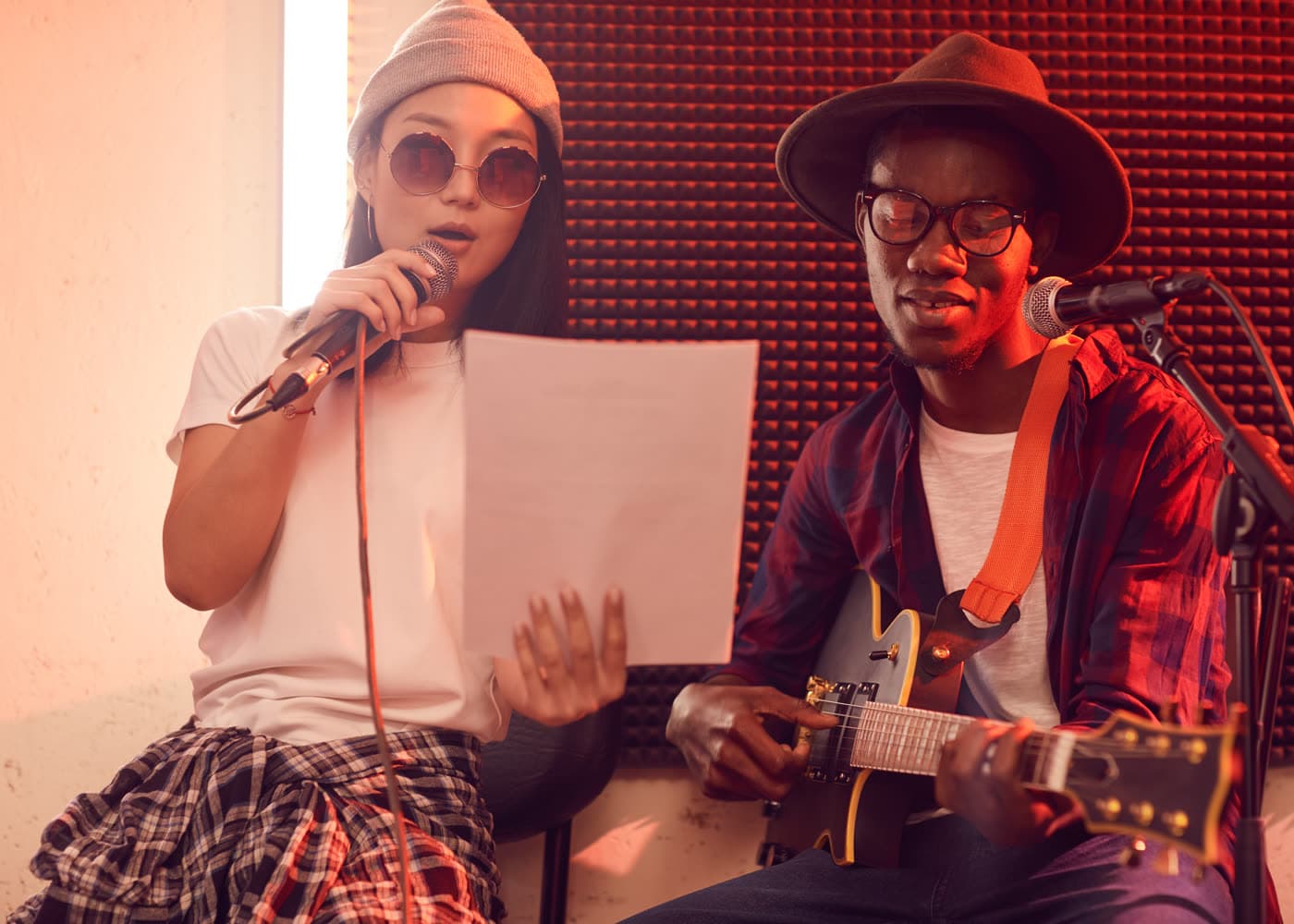 Musical duo singing and playing guitar in a dim studio